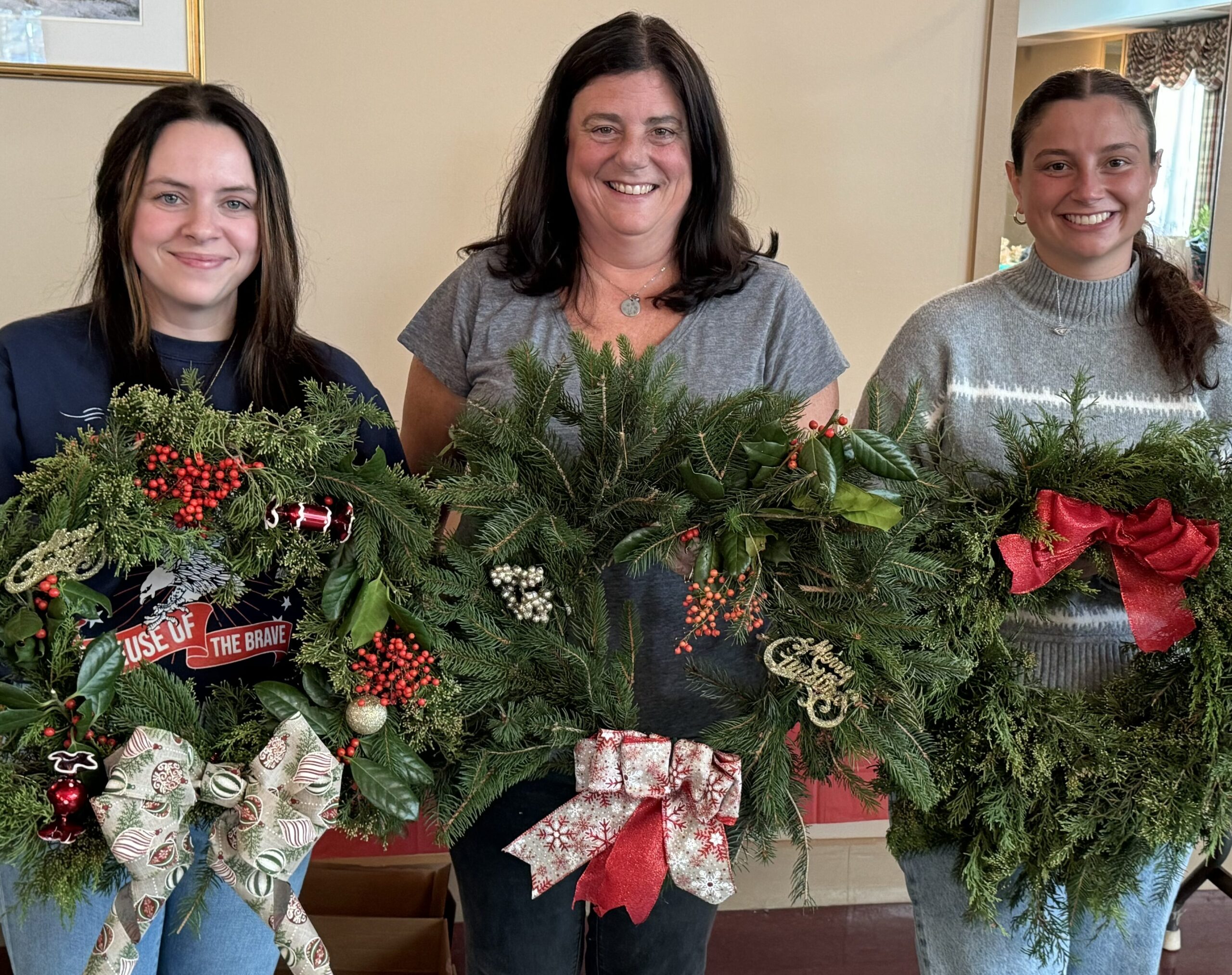 Three women holding the wreaths they made at the Wine & Wreath making event in November 2024.